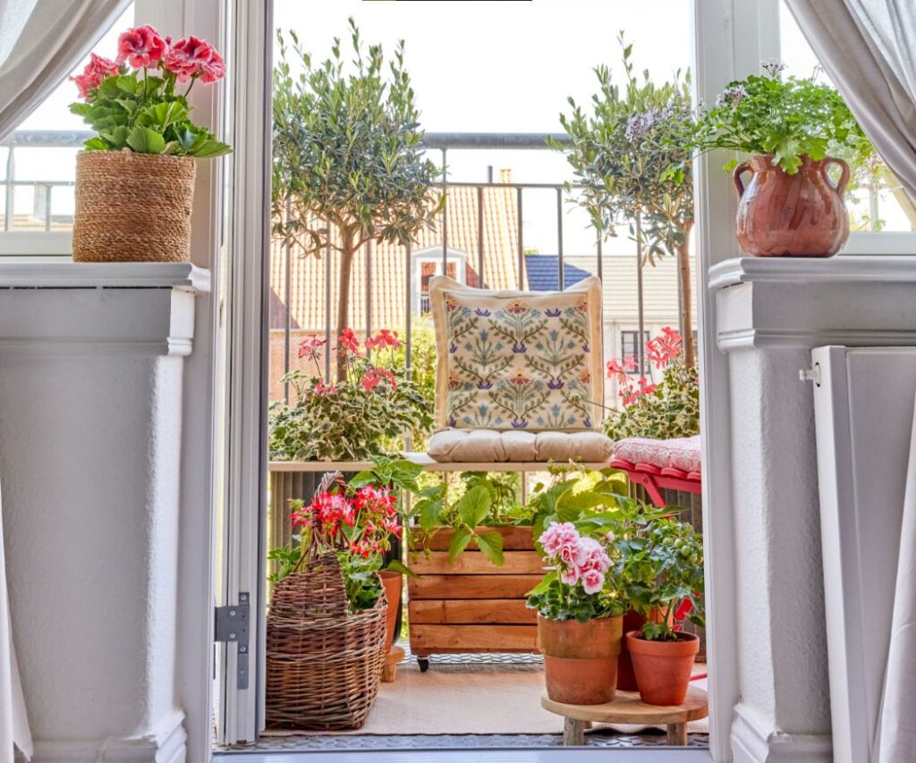Ein kleiner Balkon, liebevoll dekoriert mit einer Mischung aus Möbeln und Geranien. Eine Holzbank mit weichen Kissen ist der Mittelpunkt, umgeben von Blumentöpfen und anderen Pflanzen. Perfekt für eine entspannende Pause.