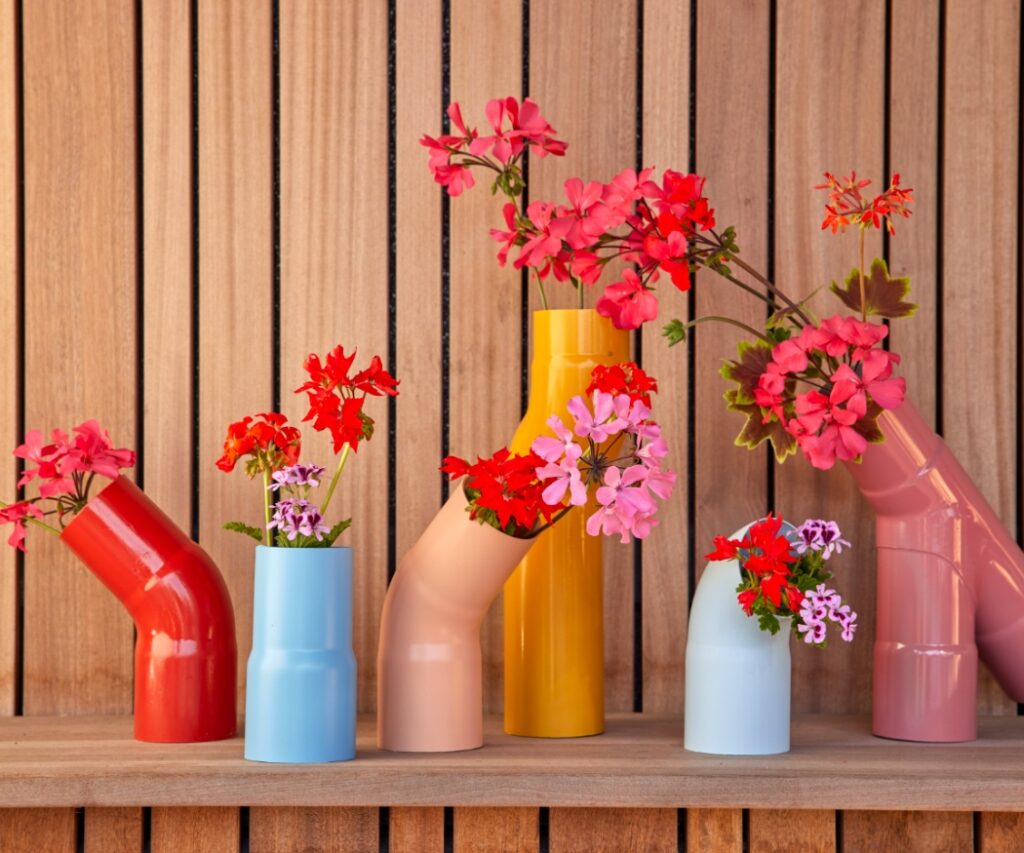 Mit wasserfester Farbe besprühte Abflussrohre aus Kunststoff sind ein origineller Blickfang und eine kreative Art, geschnittene Geranien in Szene zu setzen.