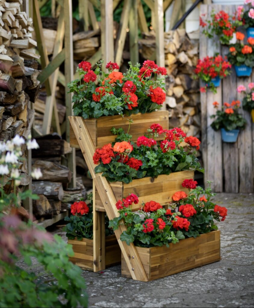 Gestapelte Holzpflanzkästen mit roten Geranien im Garten – platzsparende Gartenidee mit vertikaler Bepflanzung