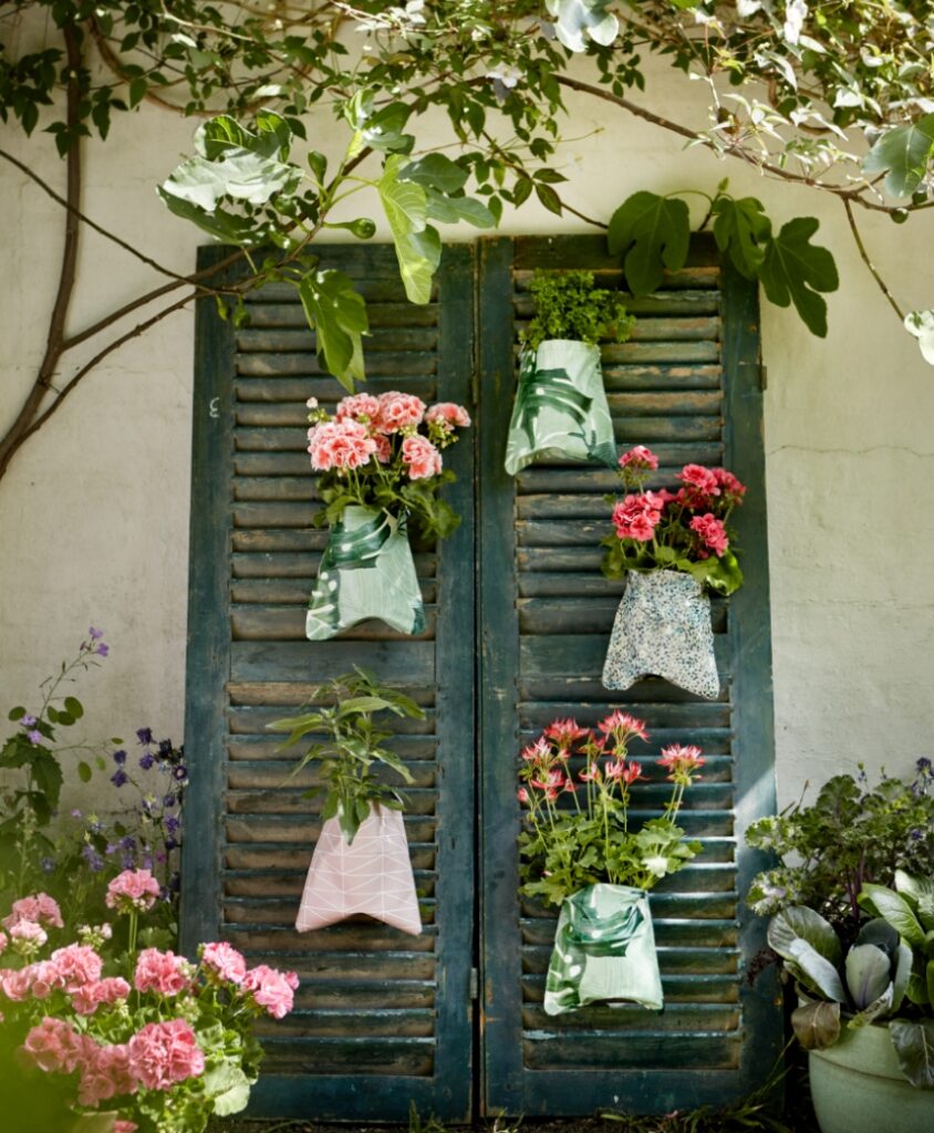 Upcycling-Idee für den Garten: alte Fensterläden mit hängenden Pflanztaschen und Geranien in Rosa und Grün