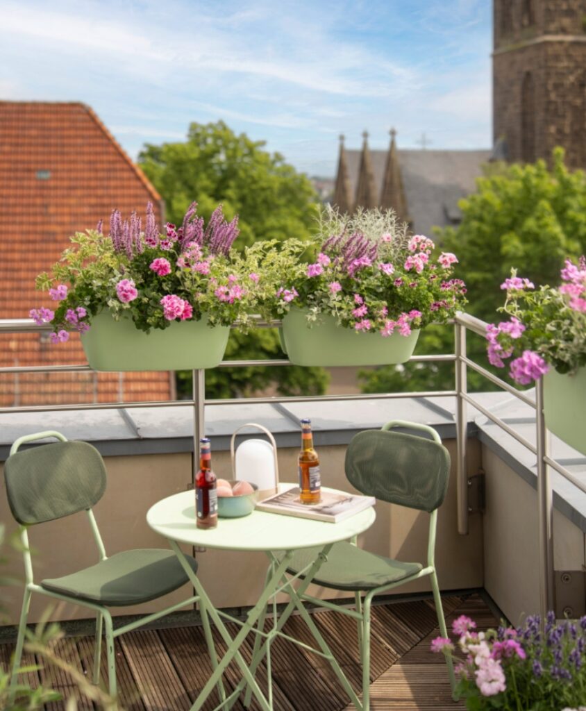 Balkon mit rosa Geranien in Balkonkästen und grünen Möbeln – harmonische Balkonidee mit wiederkehrenden Farben